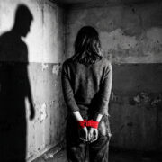 Mujer atada con cinta roja y sombra masculina amenazante: Metáfora de la violencia de género y el patriarcado.