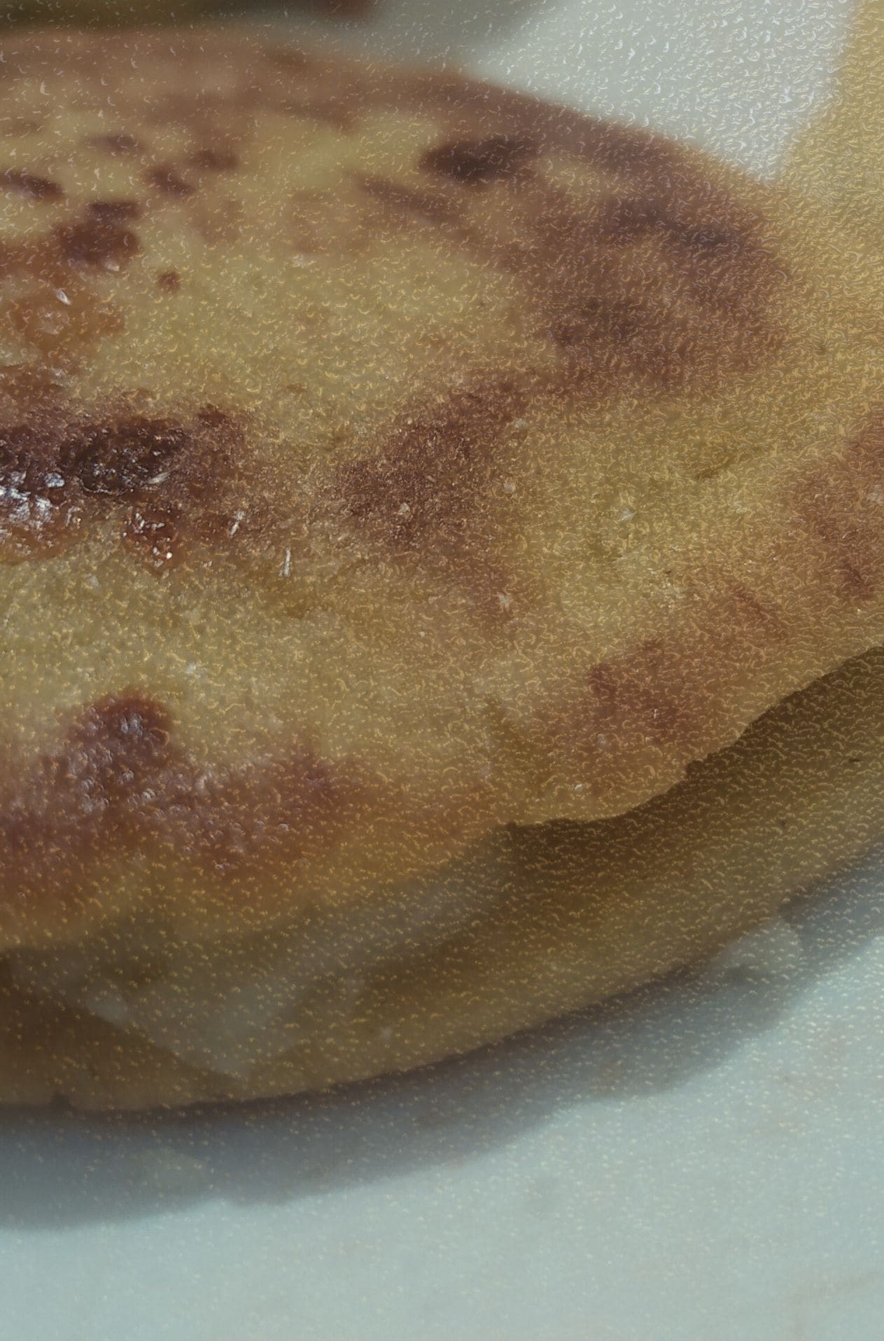 Primer plano de una arepa de plátano maduro asada con queso derretido en su interior. La imagen destaca las marcas doradas de la cocción y la textura granulada, formando parte del archivo de bodegones populares KOKOGOA.