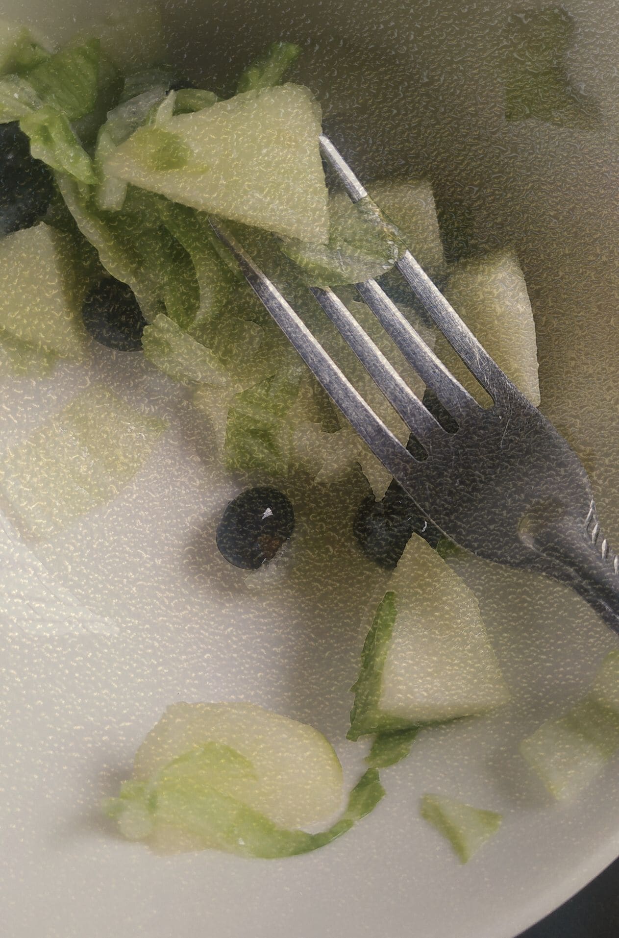 Plano detalle de un bowl blanco con ensalada de manzana verde, lechuga y arándanos, con un tenedor de metal. Fotografía cinematográfica que captura un momento de mesa cotidiano en el archivo de alimentación real KOKOGOA.
