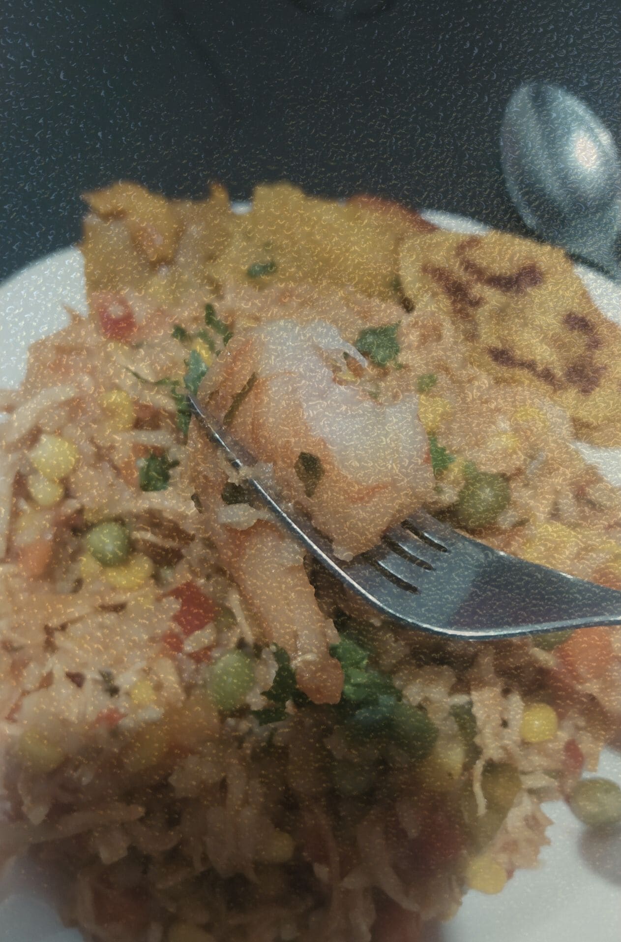 Primer plano de un tenedor sosteniendo un camarón sobre un plato de arroz con especias, verduras y patacón. Una imagen del archivo KOKOGOA que documenta la cena como un ritual de identidad sensorial y alimentación real.