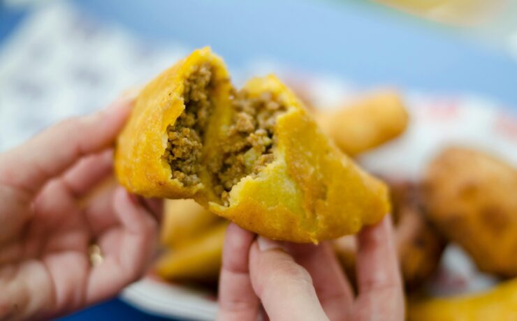 Crónica de la empanada colombiana: Primer plano de una empanada de maíz dorado abierta por la mitad, revelando un relleno jugoso de carne picada y vapor ascendente. La fotografía de Frederick Medina captura la textura crujiente y la esencia de la cocina callejera tradicional.