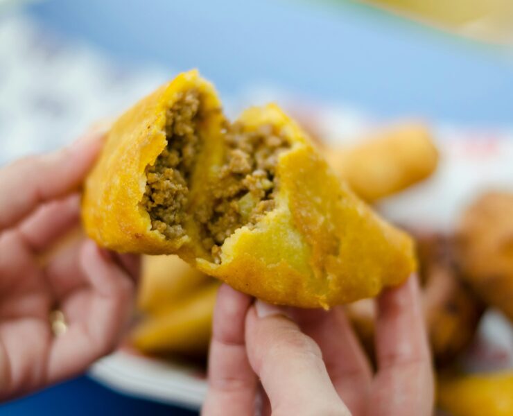 Crónica de la empanada colombiana: Primer plano de una empanada de maíz dorado abierta por la mitad, revelando un relleno jugoso de carne picada y vapor ascendente. La fotografía de Frederick Medina captura la textura crujiente y la esencia de la cocina callejera tradicional.