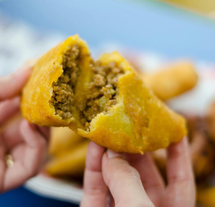 Crónica de la empanada colombiana: Primer plano de una empanada de maíz dorado abierta por la mitad, revelando un relleno jugoso de carne picada y vapor ascendente. La fotografía de Frederick Medina captura la textura crujiente y la esencia de la cocina callejera tradicional.