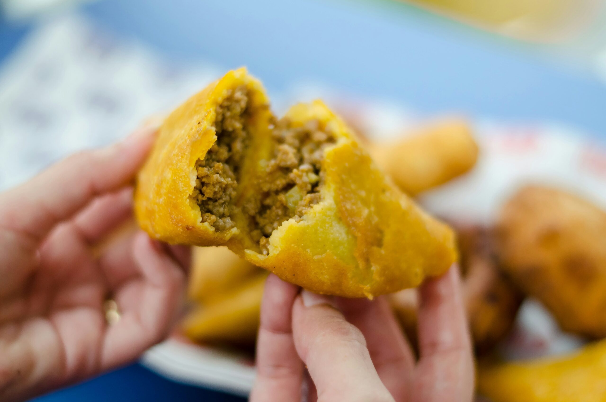 Crónica de la empanada colombiana: Primer plano de una empanada de maíz dorado abierta por la mitad, revelando un relleno jugoso de carne picada y vapor ascendente. La fotografía de Frederick Medina captura la textura crujiente y la esencia de la cocina callejera tradicional.