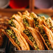 Baklava en Estambul: Foto en primer plano de filas de baklava turca dispuestas en una bandeja metálica de horno. Se aprecian las finas capas de masa filo en color dorado crujiente y el intenso relleno de pistacho picado.