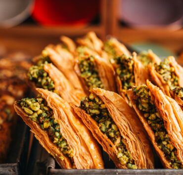 Baklava en Estambul: Foto en primer plano de filas de baklava turca dispuestas en una bandeja metálica de horno. Se aprecian las finas capas de masa filo en color dorado crujiente y el intenso relleno de pistacho picado.