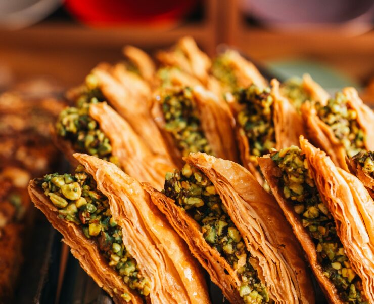 Baklava en Estambul: Foto en primer plano de filas de baklava turca dispuestas en una bandeja metálica de horno. Se aprecian las finas capas de masa filo en color dorado crujiente y el intenso relleno de pistacho picado.