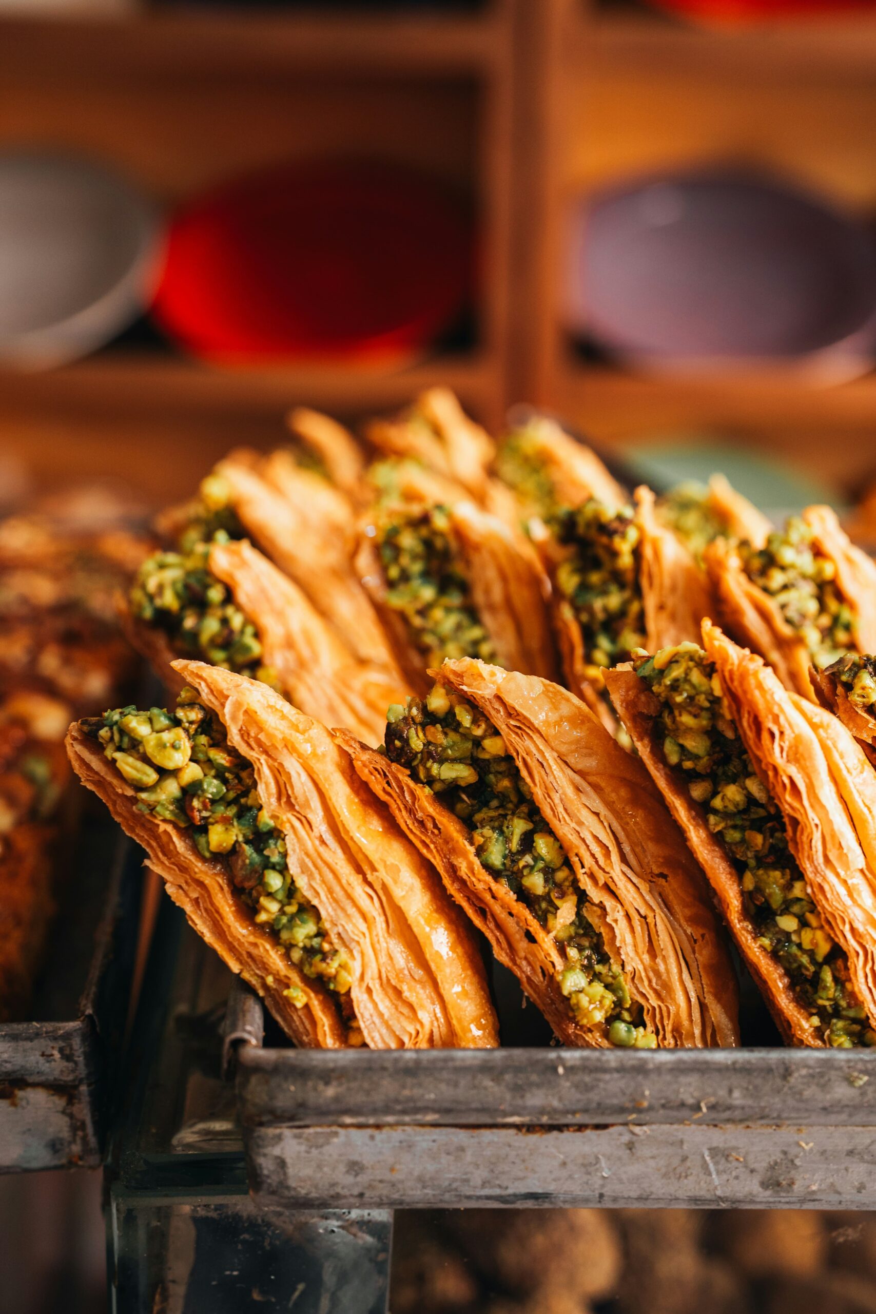 Baklava en Estambul: Foto en primer plano de filas de baklava turca dispuestas en una bandeja metálica de horno. Se aprecian las finas capas de masa filo en color dorado crujiente y el intenso relleno de pistacho picado.