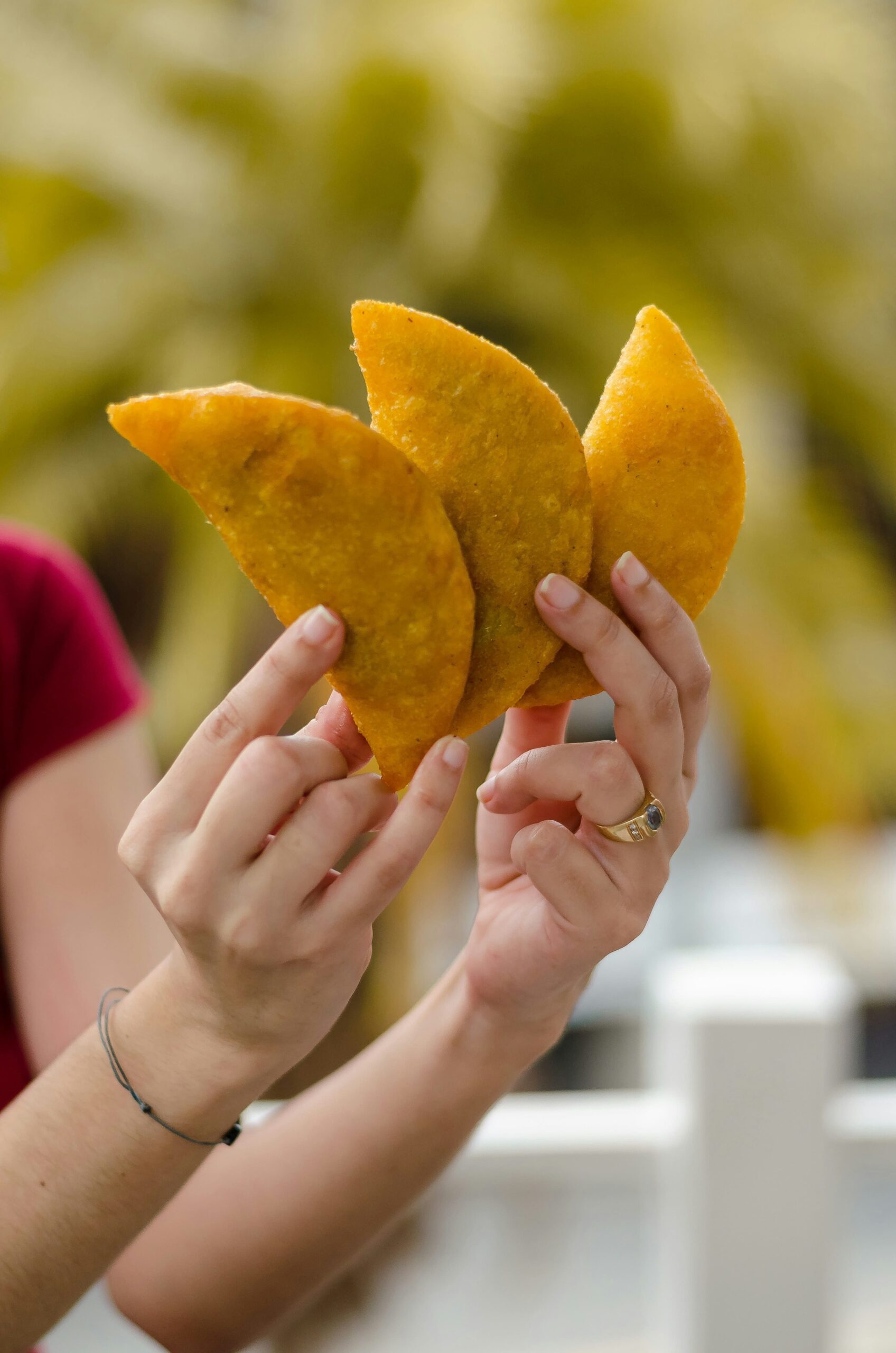 Empanada colombiana: Una mano sostiene tres empanadas de maíz recién fritas, de color amarillo intenso y textura crujiente. El fondo desenfocado resalta la forma de media luna perfecta de este alimento tradicional. Fotografía de Frederick Medina.