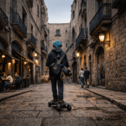 Simón en Barcelona: Imagen de un joven de 22 años con cabello azul turquesa, visto de espaldas mientras recorre en monopatín un callejón gótico del barrio del Born. Lleva una guitarra eléctrica negra colgada y audífonos, rodeado de fachadas de piedra y balcones de hierro.