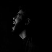 Fotografía en blanco y negro de alto contraste que muestra el perfil de un hombre con barba gritando con fuerza hacia la oscuridad. La iluminación lateral resalta la expresión de angustia y desahogo sobre un fondo completamente negro. Una representación visual del dolor y el vacío que deja un amor imaginario.