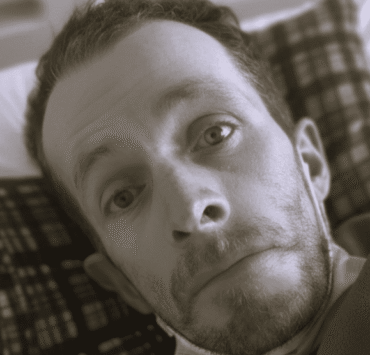 Herencia del alma: primer plano en blanco y negro de un hombre de mirada noble y profunda, con ojos claros que reflejan serenidad y una leve sonrisa; la iluminación suave resalta la paz de su expresión, simbolizando la herencia espiritual y el amor inquebrantable que trasciende la pérdida física.