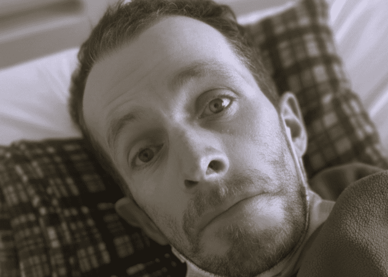 Herencia del alma: primer plano en blanco y negro de un hombre de mirada noble y profunda, con ojos claros que reflejan serenidad y una leve sonrisa; la iluminación suave resalta la paz de su expresión, simbolizando la herencia espiritual y el amor inquebrantable que trasciende la pérdida física.