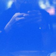 Identidad digital: retrato abstracto en tonos azules saturados de una silueta humana difusa frente a un dispositivo móvil. El fuerte grano fotográfico y el resplandor de la pantalla crean una atmósfera eléctrica donde los rasgos físicos desaparecen, dejando solo la forma del sujeto interactuando con la tecnología.